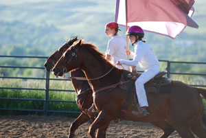  Madison Hawkinson and a teammate practicing formation riding with flags at a gallop